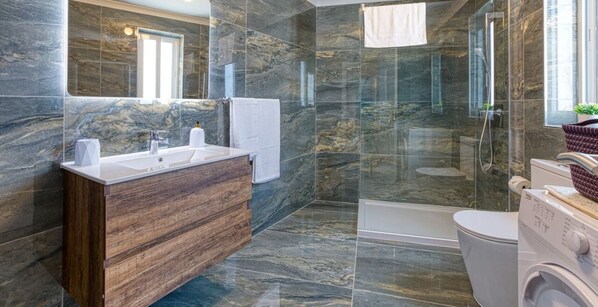 Un bagno moderno con una parete in marmo, un mobile lavabo in legno, una cabina doccia in vetro e una lavatrice integrata.