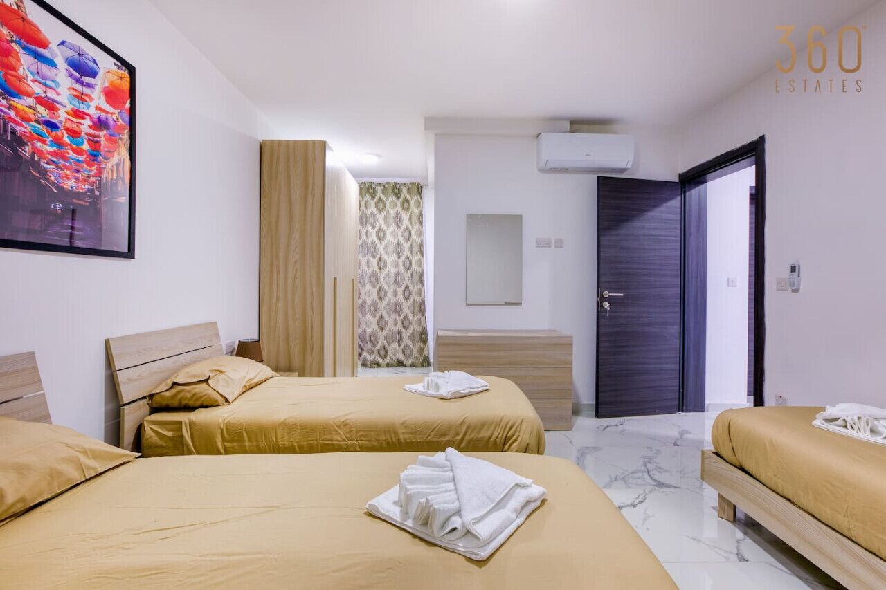 Een hotelkamer met twee bedden, een groot schilderij, een airconditioning en een deur naar een andere kamer.