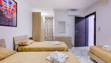 Een hotelkamer met twee bedden, een groot schilderij, een airconditioning en een deur naar een andere kamer.