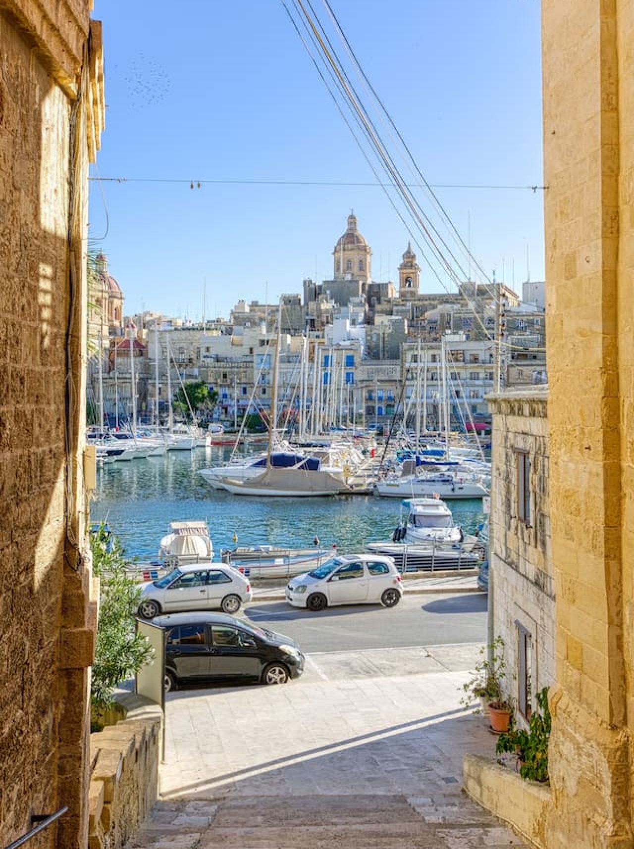 A marina with boats docked, a clear sky, and buildings in the background.