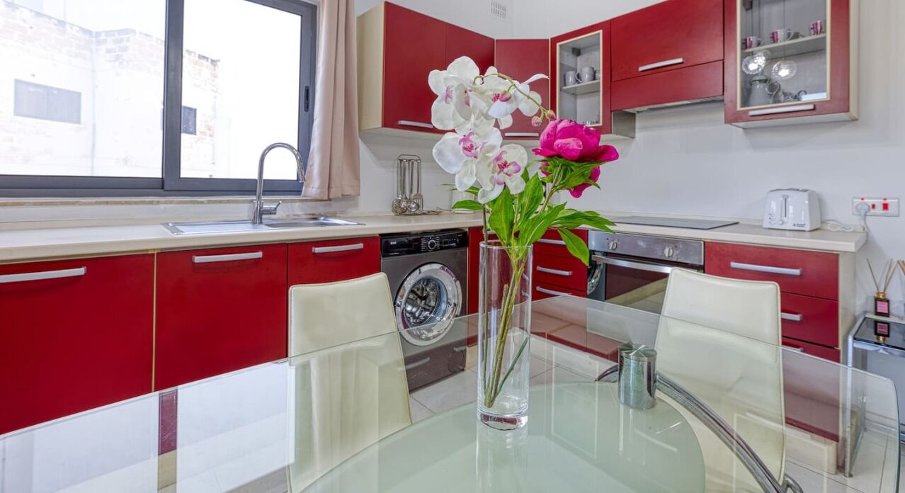 Una cocina moderna con armarios rojos, una mesa de vidrio y un florero con flores.