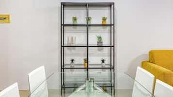 Une salle de conférence avec une table en verre, des chaises blanches, un canapé jaune et une étagère noire où sont disposées des plantes en pot.