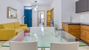Una sala de estar moderna con una mesa de comedor de vidrio, un sofá amarillo y una cocina con armarios de madera.