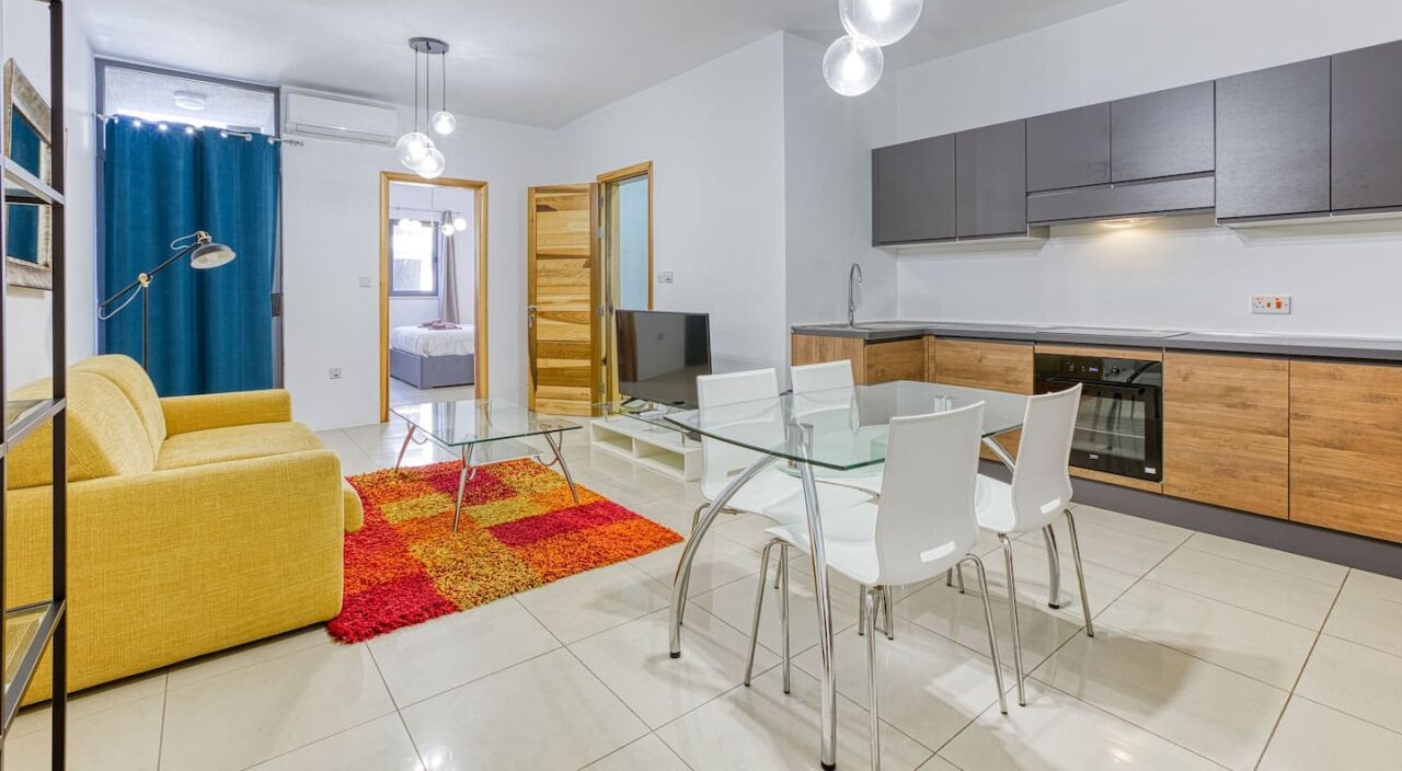 Un salon moderne avec une table à manger en verre, des chaises blanches, un canapé jaune et un tapis rouge et orange.
