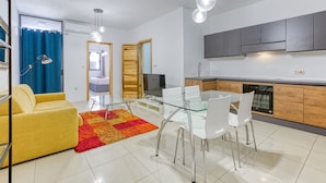 Una sala de estar moderna con una mesa de comedor de vidrio, sillas blancas, un sofá amarillo y una alfombra roja y naranja.