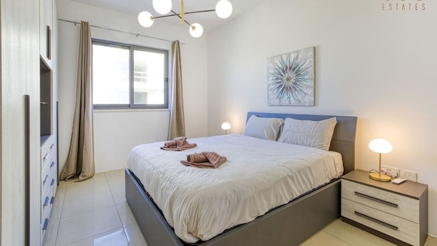 Un dormitorio moderno con cama, mesitas de noche, lámpara de techo y ventana con cortinas.