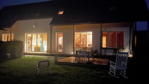 Ein modernes Haus mit Terrasse, Essbereich und sichtbarer Küche durch die Fenster.