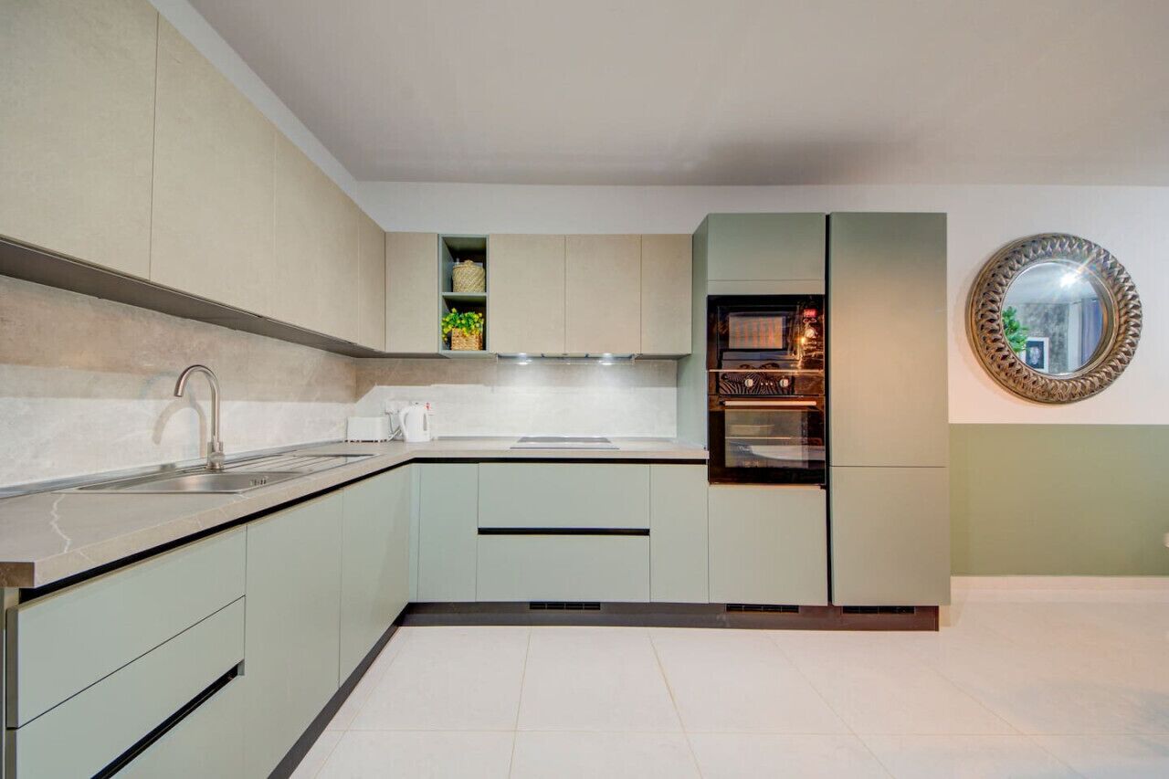 A modern kitchen with light green cabinets, a stainless steel sink, and a built-in oven.