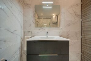 A bathroom with a marble-tiled wall, a white sink with a mirror above it, and a towel dispenser. - Modern 2BR home with modern amenities in Gzira (Il-Gżira)