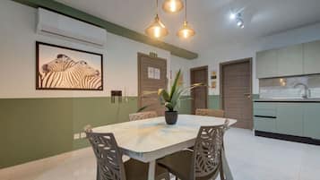 Een eetruimte met een ronde tafel, stoelen en hanglampen. Aan de muur hangt een lijst met een afbeelding van een zebra en op de tafel staat een potplant.