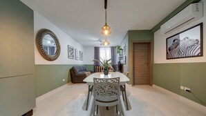 Un coin repas avec une table et des chaises blanches, un luminaire suspendu et un tableau représentant une zèbre, accroché au mur.