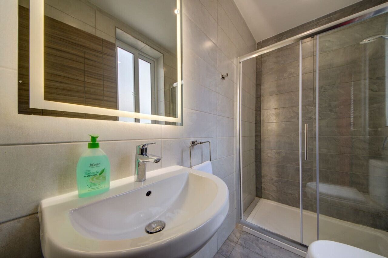 Een moderne badkamer met een witte wastafel, een spiegel en een douchecabine met glazen wanden.