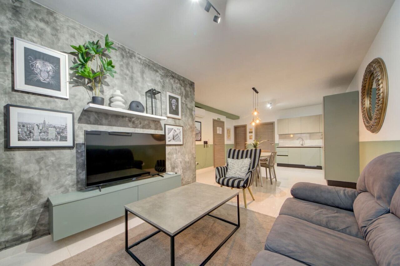 Un salon moderne avec un téléviseur à écran plat, un canapé gris, un fauteuil à rayures et une table basse.