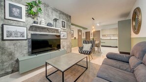 Un salon moderne avec un téléviseur à écran plat, un canapé gris, un fauteuil à rayures et une table basse.