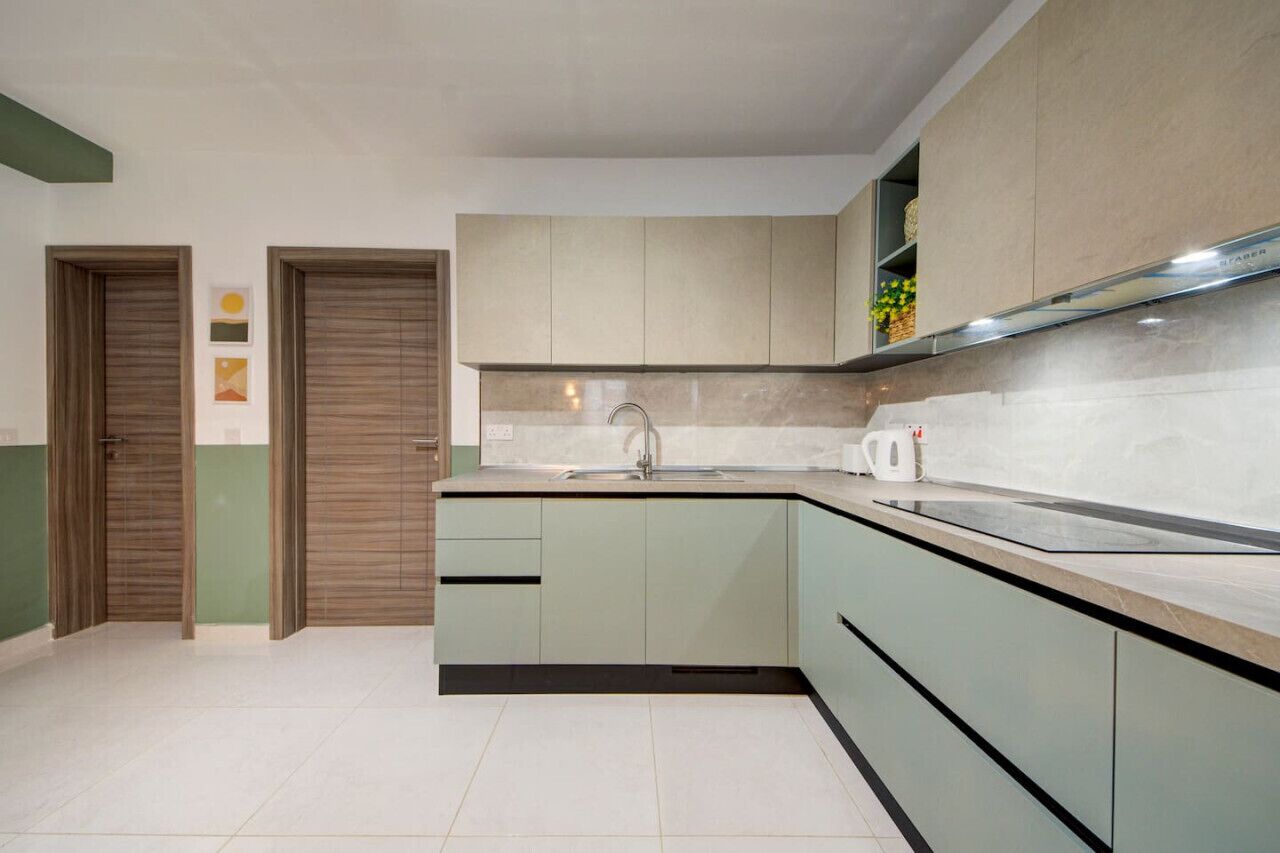 A modern kitchen with light green cabinets, a white countertop, and a stainless steel range hood.