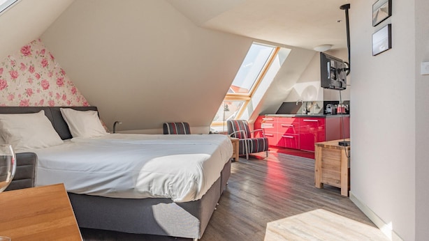 Ein Schlafzimmer mit einem Bett, einem Schreibtisch und einem Stuhl. Es gibt eine Küchenzeile mit roten Schränken und einem Fenster.