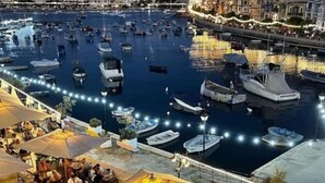 Een jachthaven met aangemeerde boten, terras met parasols en een stadsgezicht op de achtergrond.