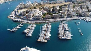 An aerial view of a marina with numerous boats docked, surrounded by residential buildings and a prominent cruise ship. - One of a kind 5BR penthouse with terrace in Pieta (Tal-Pietà)