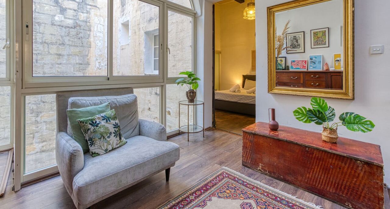 Un salon chaleureux avec un canapé gris, une console en bois et une grande fenêtre donnant sur un mur en pierre.