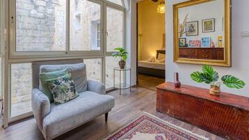 Un salon chaleureux avec un canapé gris, une console en bois et une grande fenêtre donnant sur un mur en pierre.