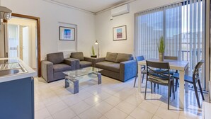 Un salon moderne avec une table basse en verre, des canapés gris, une table à manger avec des chaises et un balcon avec vue.