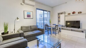 A modern living room with a sofa, coffee table, and a TV. There is a dining area with chairs and a table.