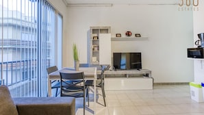 A modern living room with a dining area, a flat-screen TV, and a potted plant.