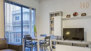 A modern living room with a dining area, a sofa, a TV, and a balcony with blinds.