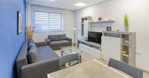 Un salón moderno con un sofá gris, una mesa de centro de cristal y un televisor de pantalla plana.