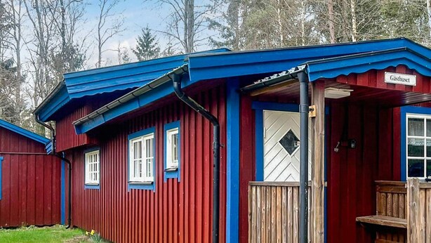 A red and blue cabin with a wooden deck and a door labeled "Gästhaus". - 6 Person Holiday Home in Bredaryd (Bredaryd)