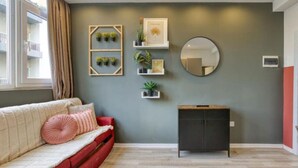 A room with a sofa, a small cabinet, and wall-mounted shelves with plants.