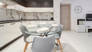 Una cocina moderna con una mesa de comedor de vidrio, armarios blancos y un salpicadero de mármol.
