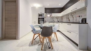 Una cocina moderna con una mesa de comedor de vidrio, armarios blancos y un salpicadero de mármol.