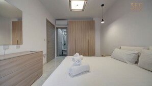 Una habitación de hotel moderna con una cama grande, un aparador de madera, un espejo y un baño visible a través de una puerta abierta.