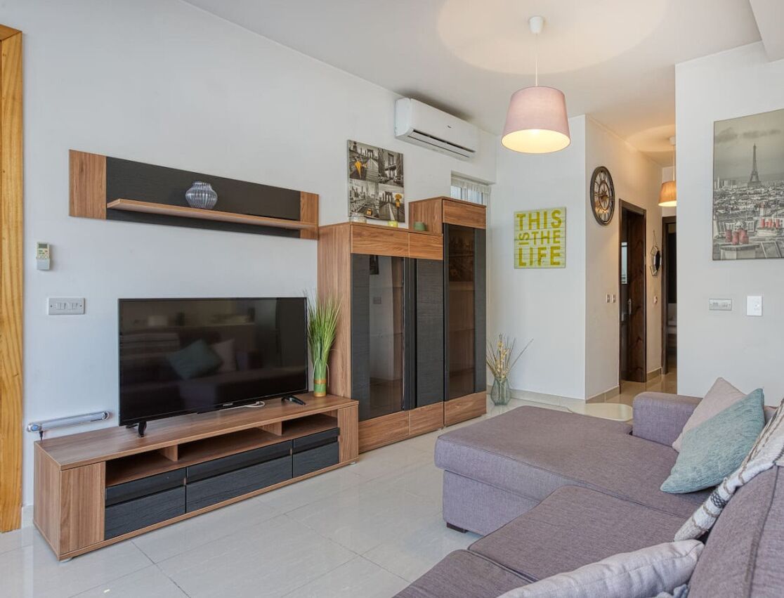 Un salon moderne avec un téléviseur à écran plat, un meuble de rangement en bois et un canapé gris.