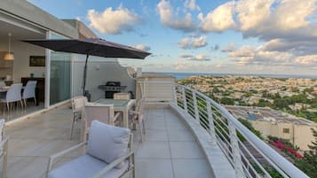 Un balcón con mobiliario exterior, una parrilla y vistas a la ciudad.