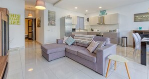 A modern living room with a sectional sofa, a dining area, and a kitchen.