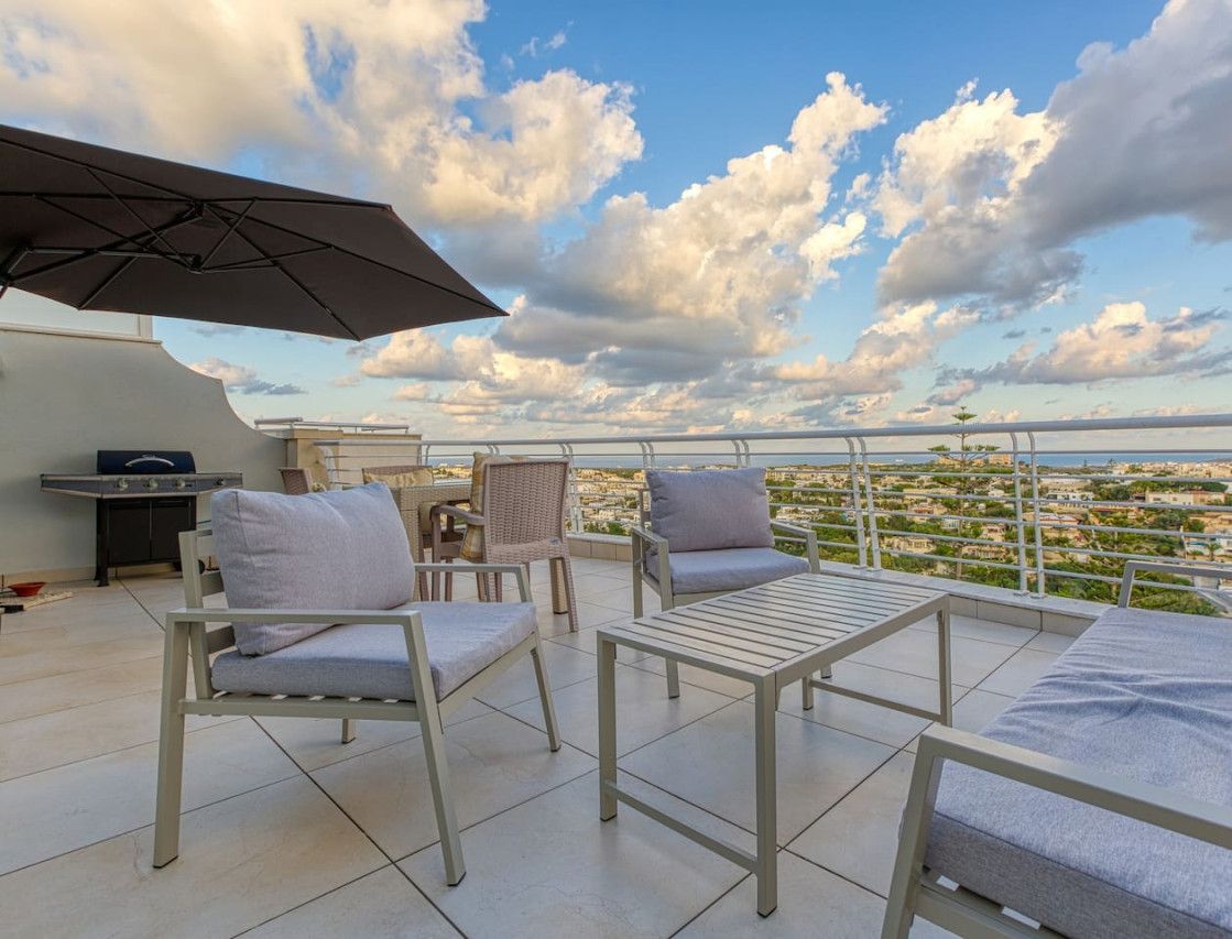 Una terraza en la azotea con mobiliario exterior, una parrilla y vistas de la ciudad.