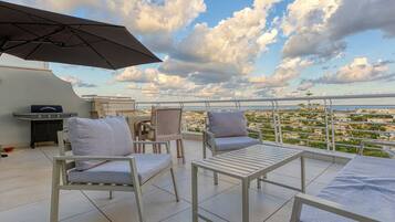 Una terraza en la azotea con mobiliario exterior, una parrilla y vistas de la ciudad.