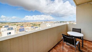 A balcony with a table and chairs, overlooking a cityscape with buildings and solar panels.