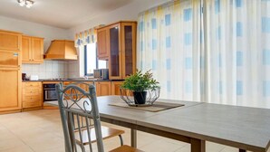 A kitchen with wooden cabinets, a dining table with chairs, a potted plant, and a window with curtains.