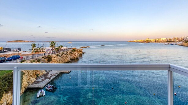 A coastal view with a clear blue sea, a rocky shoreline, and a cityscape in the background.