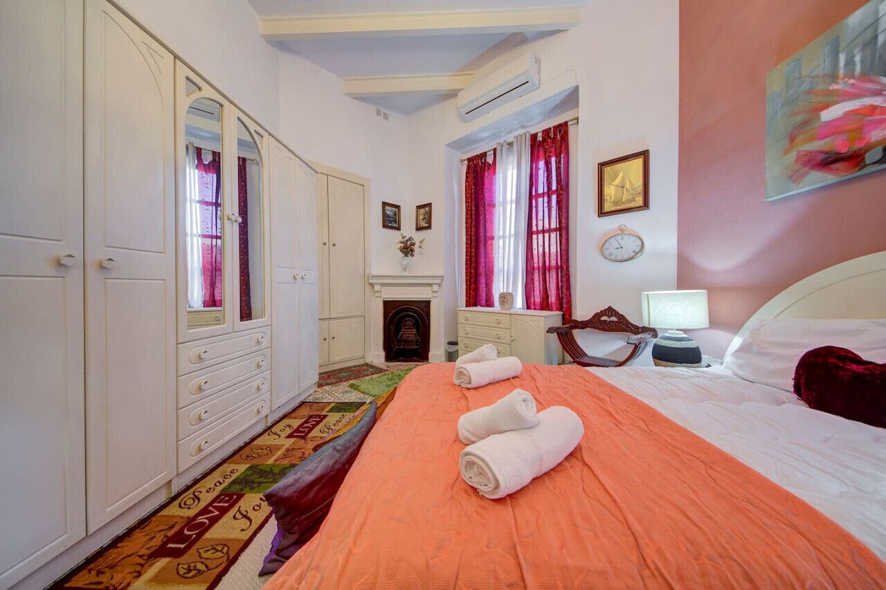 A bedroom with a bed, a wardrobe, a desk, and a fireplace.