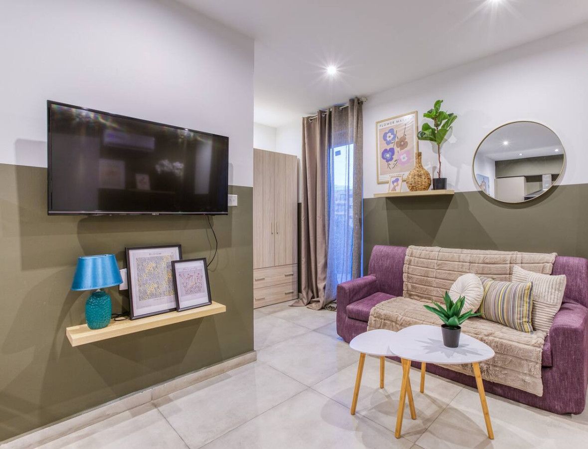 Een moderne woonkamer met een flatscreen televisie, een bank, een salontafel en een kleine plant.