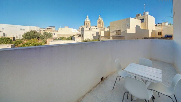A rooftop terrace with a white table and chairs, overlooking a cityscape with buildings and a church. - Traditional Maltese Escape with Rooftop Terrace! (Ħad-Dingli)