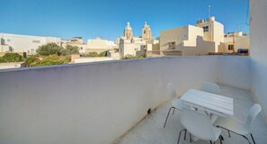 A rooftop terrace with a white table and chairs, overlooking a cityscape with buildings and a church. - Traditional Maltese Escape with Rooftop Terrace! (Ħad-Dingli)