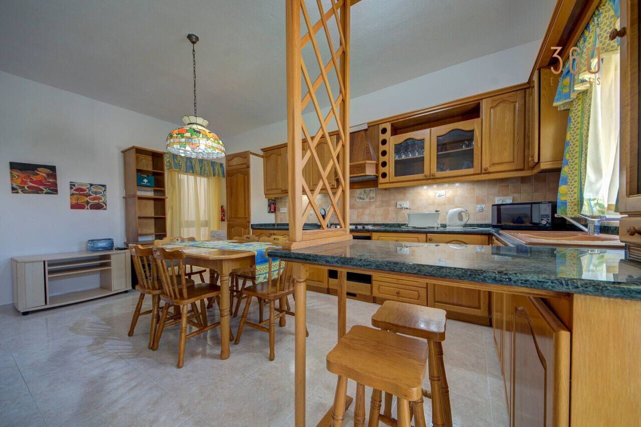 A kitchen with wooden cabinets, a granite countertop, and a dining area with wooden chairs.