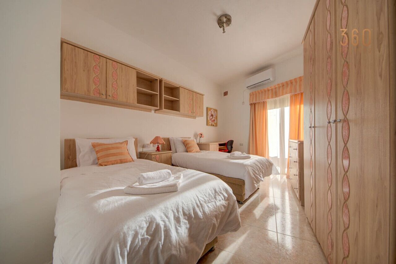 A hotel room with two beds, a wooden wardrobe, and a window with curtains.