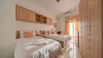 A hotel room with two beds, a wooden wardrobe, and a window with curtains.