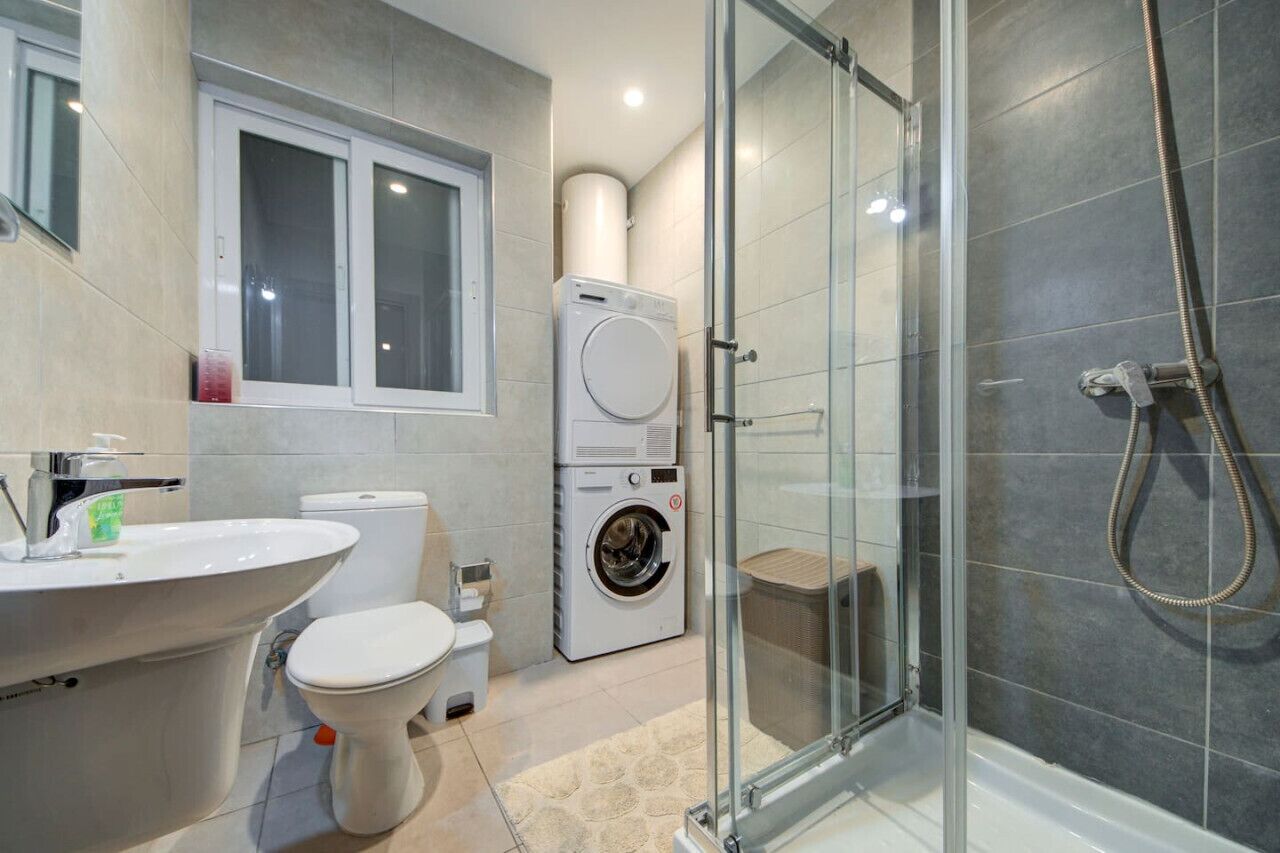 Un bagno moderno con doccia vetrata, lavatrice integrata e servizi igienici.